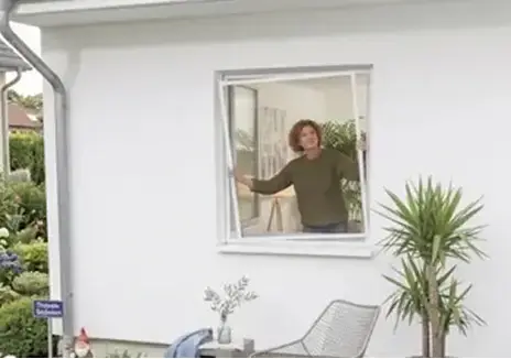 Frau an einem geöffneten Fenster mit maßgefertigtem Fliegengitter-Spannrahmen BS 1/1