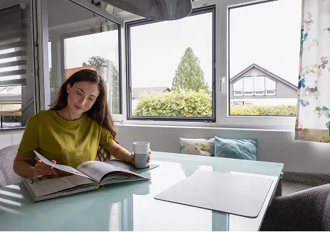 Frau liest an einem Tisch vor geöffneten Fenstern mit maßgefertigtem Fliegengitter