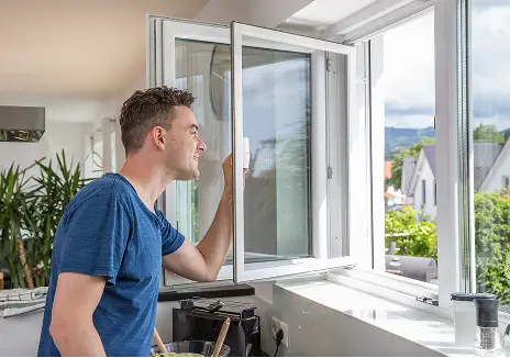 Fliegengitter-Drehfenster nach Maß für die Küche Mann öffnet ein maßgefertigtes Fliegengitter-Drehfenster am Küchenfenster