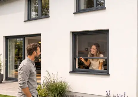 Fliegengitter-Rollo am Fenster für flexiblen Insektenschutz Frau öffnet ein Fliegengitter-Rollo am Fenster, während ein Mann davor steht
