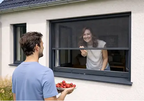 Fliegengitter-Rollo am Fenster - flexibler Insektenschutz Frau öffnet ein Fliegengitter-Rollo am Fenster, während ein Mann draußen Tomaten hält