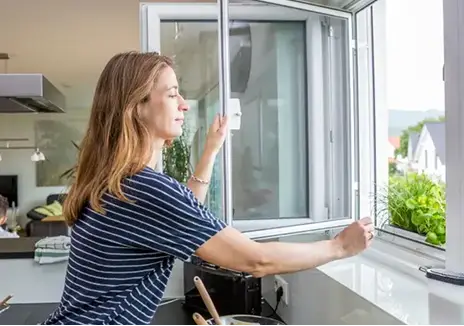 Frau öffnet ein maßgefertigtes Fliegengitter-Drehfenster am Küchenfenster