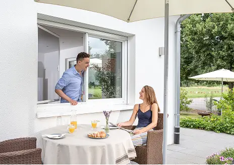 Fliegengitter am Fenster für Terrasse und Garten Mann steht an einem geöffneten Fenster mit Fliegengitter, während eine Frau auf der Terrasse sitzt