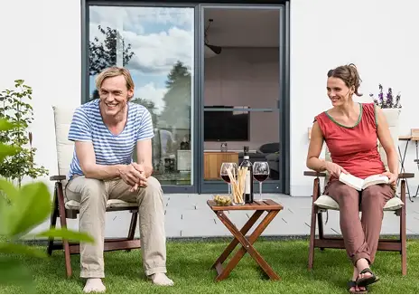 Zwei Personen sitzen auf der Terrasse vor einer Tür mit maßgefertigter Fliegengitter-Drehtür DT 3/1