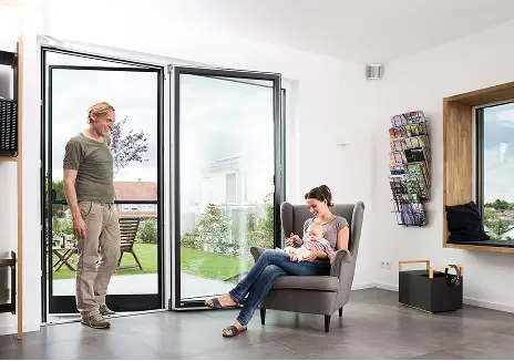 Familie im Wohnzimmer neben einer geöffneten Terrassentür mit maßgefertigter Fliegengitter-Pendeltür