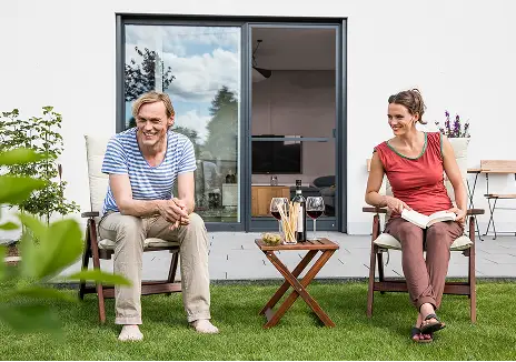 Zwei Personen sitzen im Garten vor einer Terrassentür mit Fliegengitter und genießen die Zeit im Freien