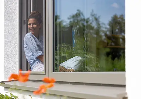 Frau sitzt an einem geöffneten Fenster mit maßgefertigtem Fliegengitterrahmen