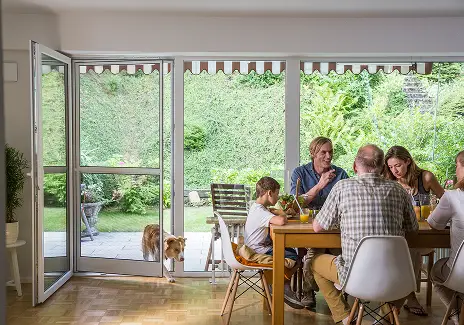 Familie sitzt am Esstisch bei geöffneter Terrassentür mit Fliegengitter-Pendeltür