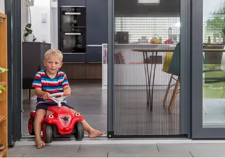 Kind fährt mit Rutschauto durch eine Terrassentür mit Insektenschutz-Plisseetür