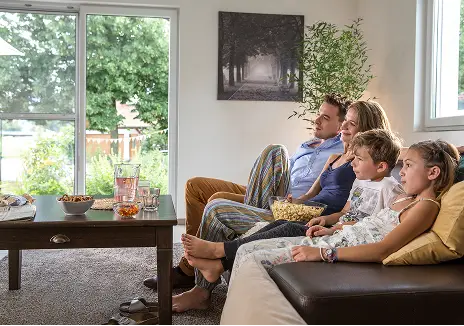 Familie sitzt gemeinsam im Wohnzimmer neben einer Terrassentür mit Fliegengitter und Blick in den Garten