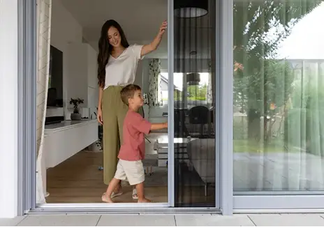 Mutter und Kind an einer Terrassentür mit Insektenschutz-Schiebetür